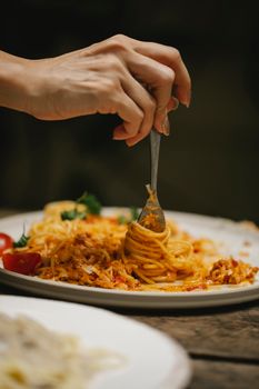 Crop anonymous female rolling delicious yummy Bolognese pasta on fork while dining in restaurant