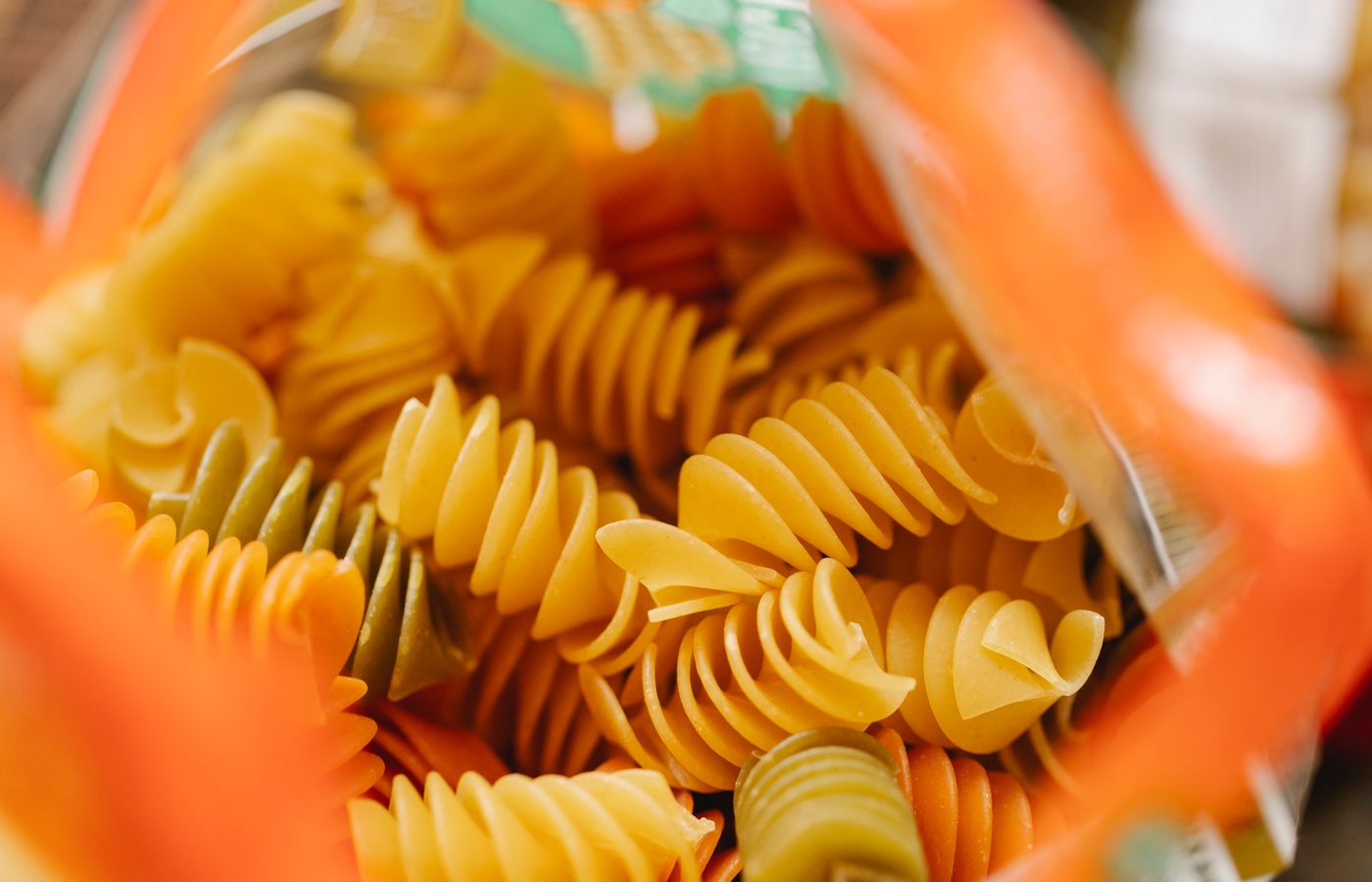 Close-up of colorful uncooked fusilli pasta inside an open bag, emphasizing its vibrant hues and texture.