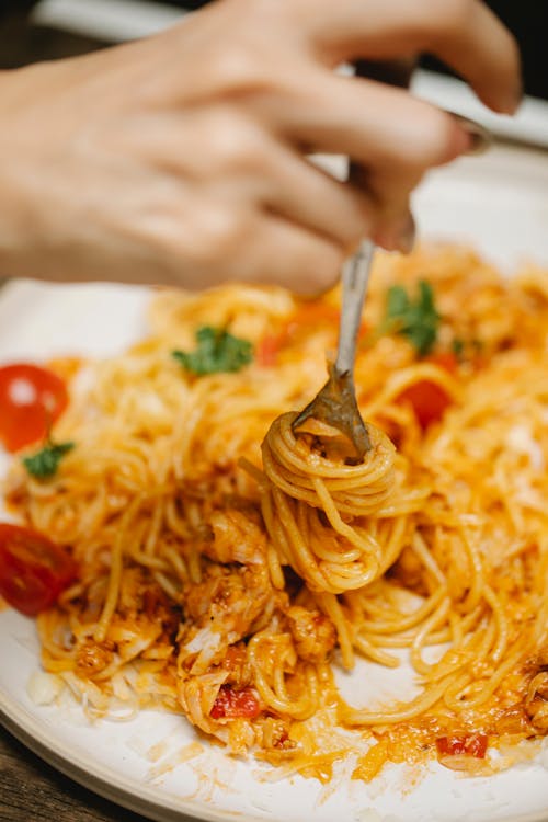 Crop anonymous person with fork eating delicious spaghetti Bolognese with cherry tomatoes and cheese and fresh basil leaves