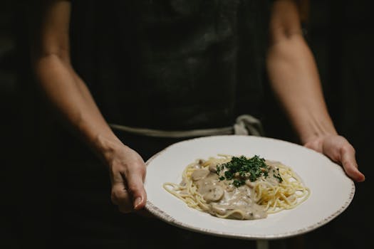 A close-up of creamy mushroom pasta held by a chef, perfect for gourmet cuisine enthusiasts.