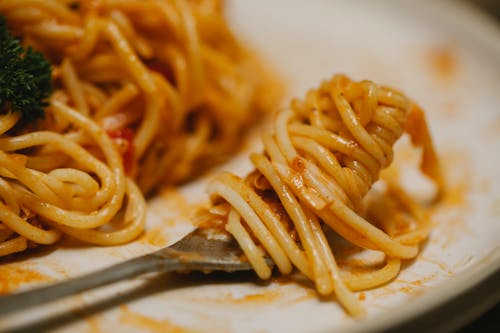 From above closeup plate and fork with appetizing spaghetti with tomato sauce and herbs served on table during lunch