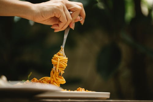 Free Crop anonymous female rolling delicious spaghetti with tomato sauce on fork during dinner in restaurant Stock Photo