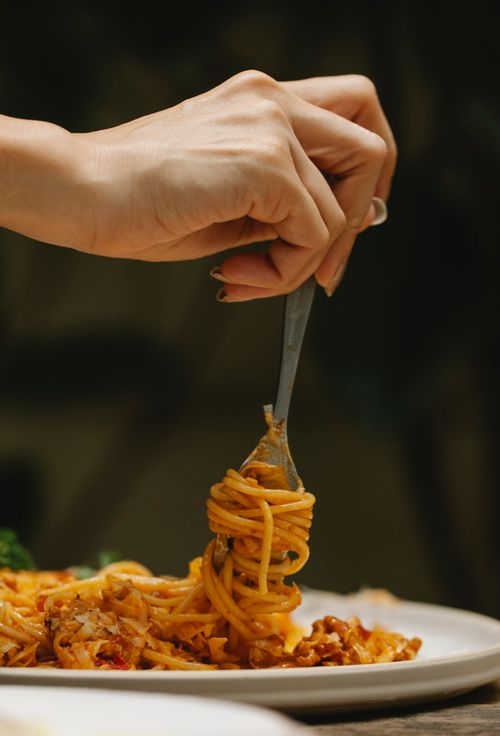 Free Crop faceless female using fork while eating yummy spaghetti alla bolognese during dinner in restaurant Stock Photo