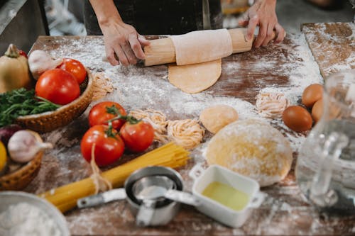 Free Woman rolling dough on table with tomatoes and eggs Stock Photo
