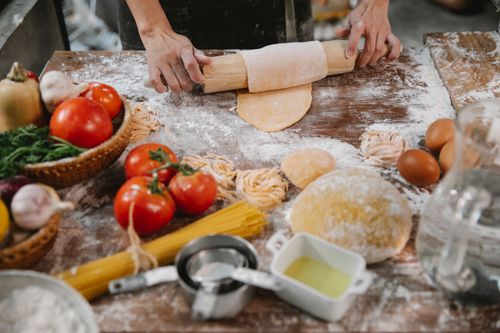 Free Crop anonymous female cooking homemade pasta on table covered with flour among vegetables Stock Photo