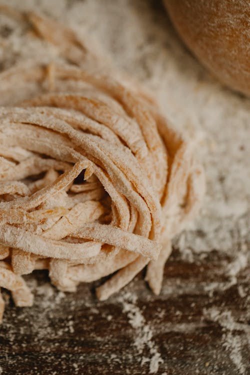 Dough of homemade fresh thin pasta placed on wooden table covered with flour
