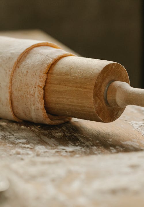 Timber rolling pin with dough and flour prepared on table in kitchen in daytime