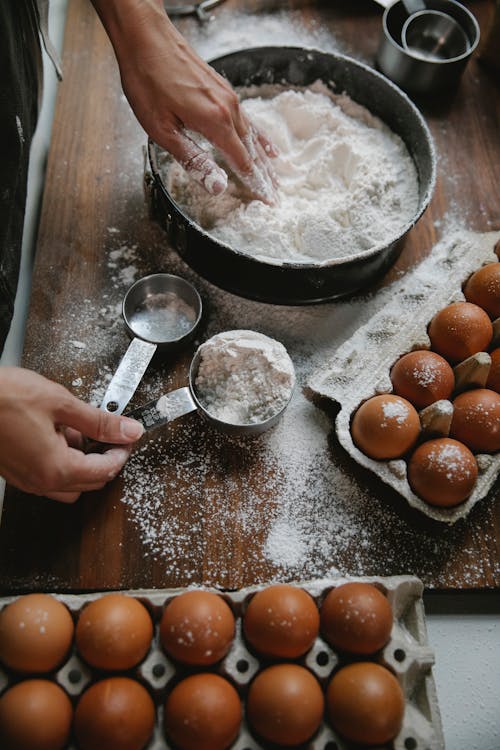 Woman cooking dough on table with eggs and flour