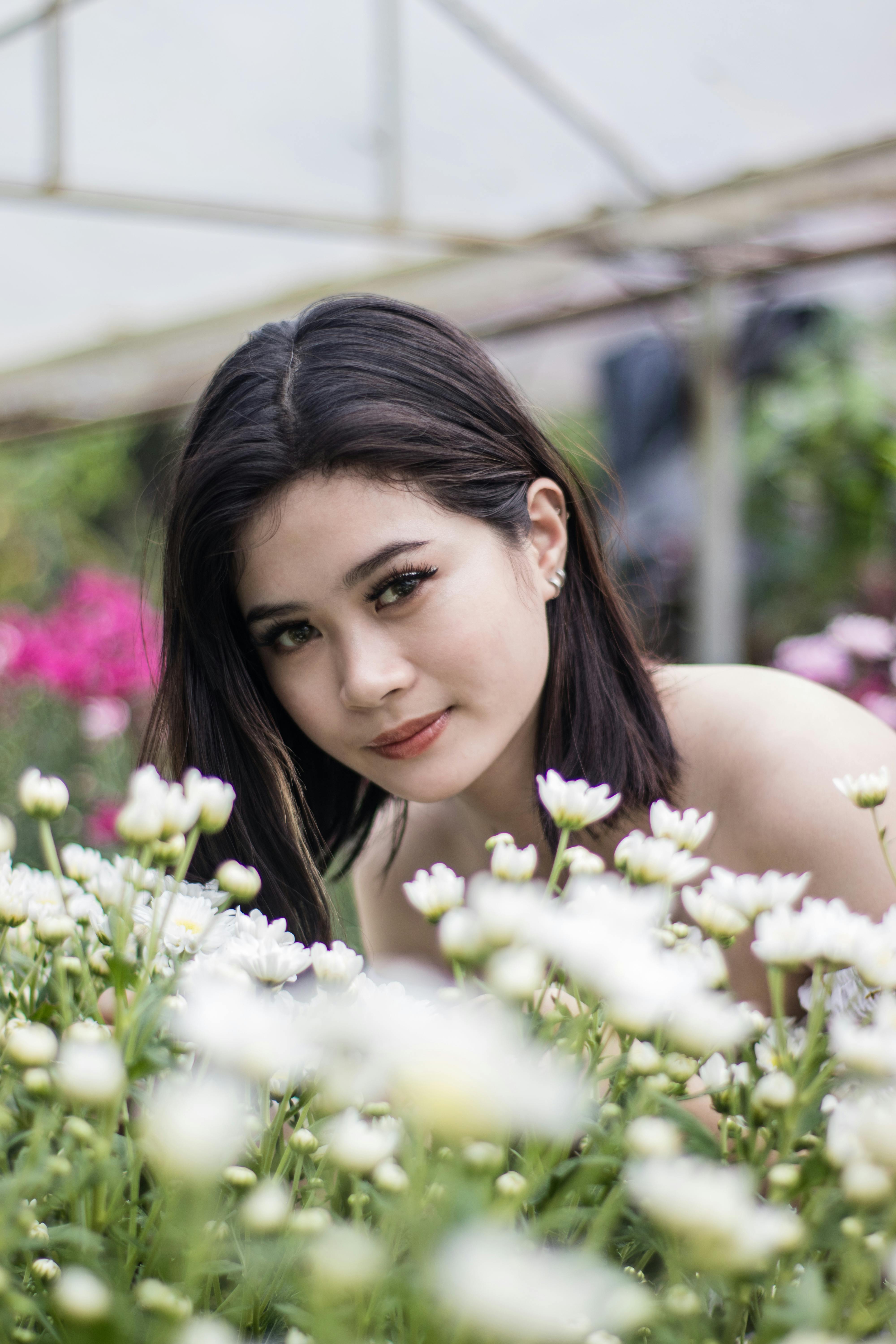 Asian woman smiling among white flowers in a vibrant garden.