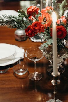 Close-up of a formal dining table setting with red floral centerpiece and candlelight.