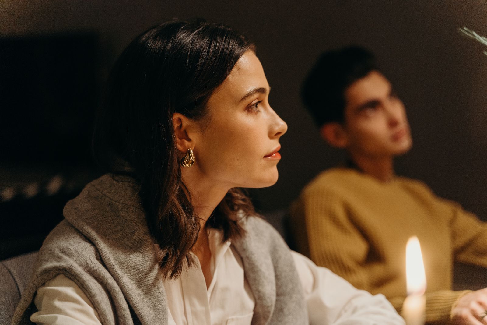 Woman in profile wearing a white collared shirt and gold earring seated in warm candlelight.