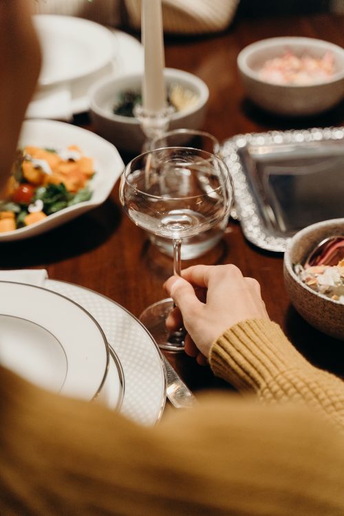 Free A person holding a crystal glass at a stylish dinner table, featuring elegant tableware. Stock Photo