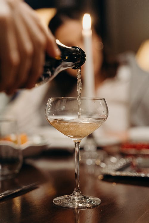 Shallow Focus Photo of a Person Pouring Champagne in a Coupe Glass