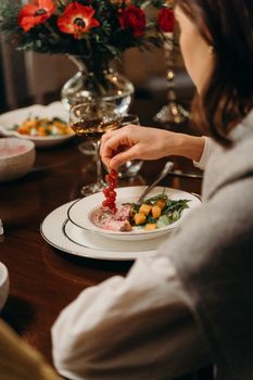 Close-up of a dining table with a person adding redcurrants to a salad, creating a gourmet dish.
