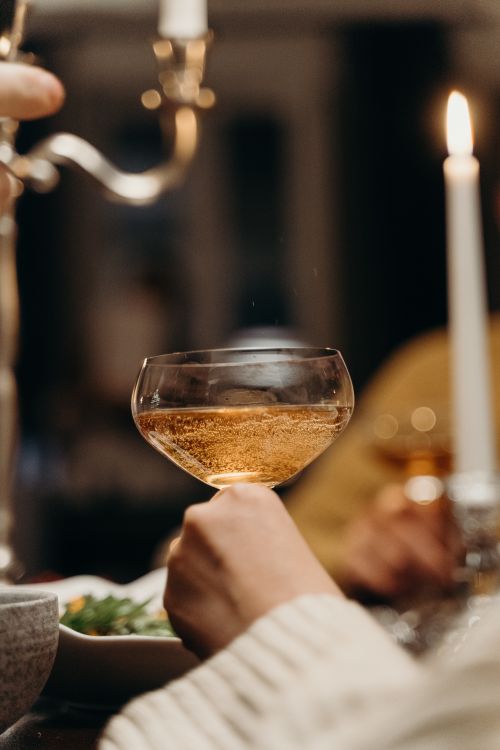 Free Close-up of a hand holding a champagne glass during a cozy candlelit dinner. Stock Photo