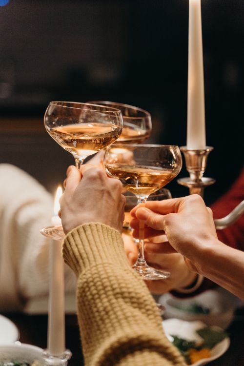Free Hands raising champagne coupe glasses in a festive toast, warmly lit setting. Stock Photo