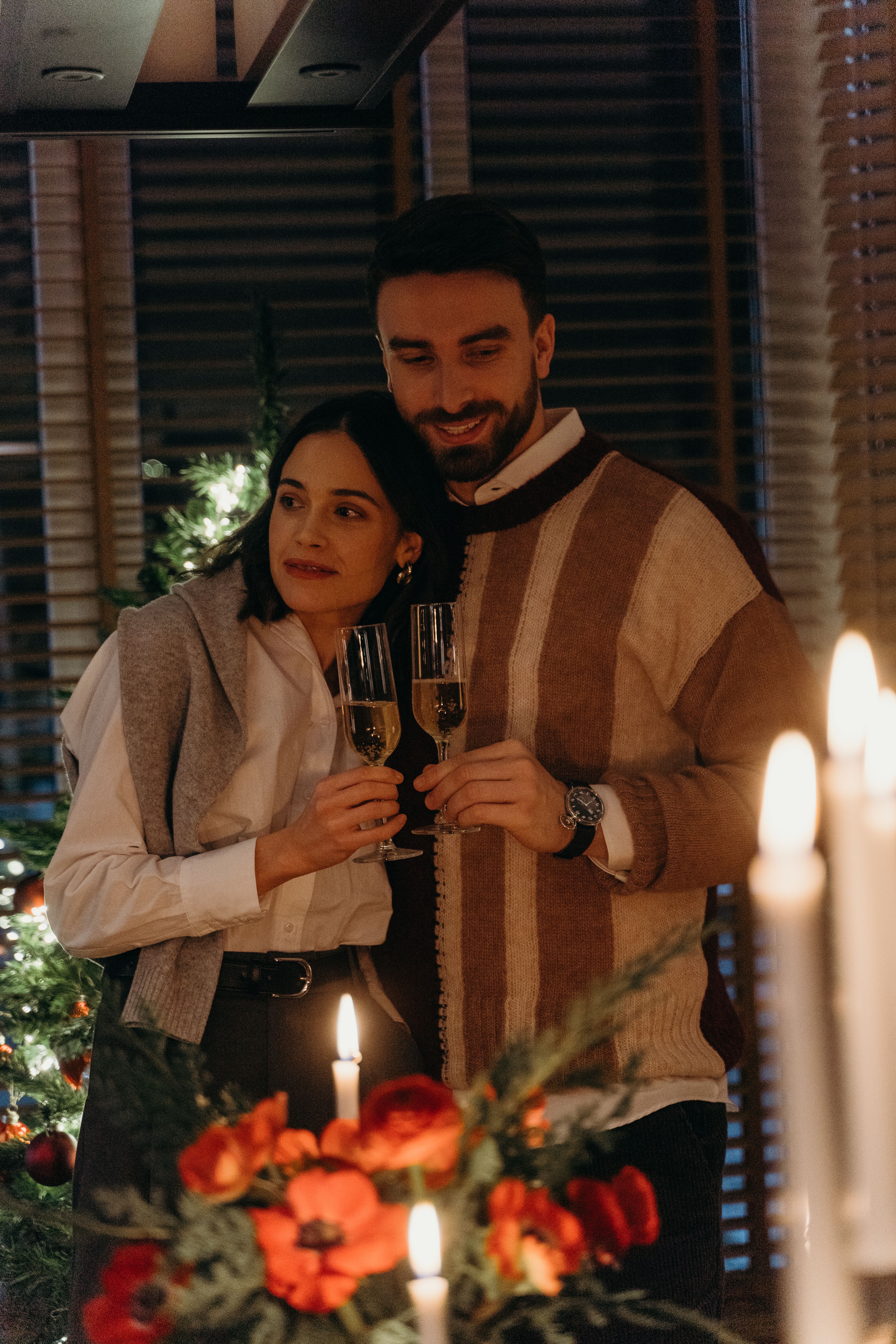 A couple enjoying a cozy celebration with champagne and candlelight indoors during the holiday season.