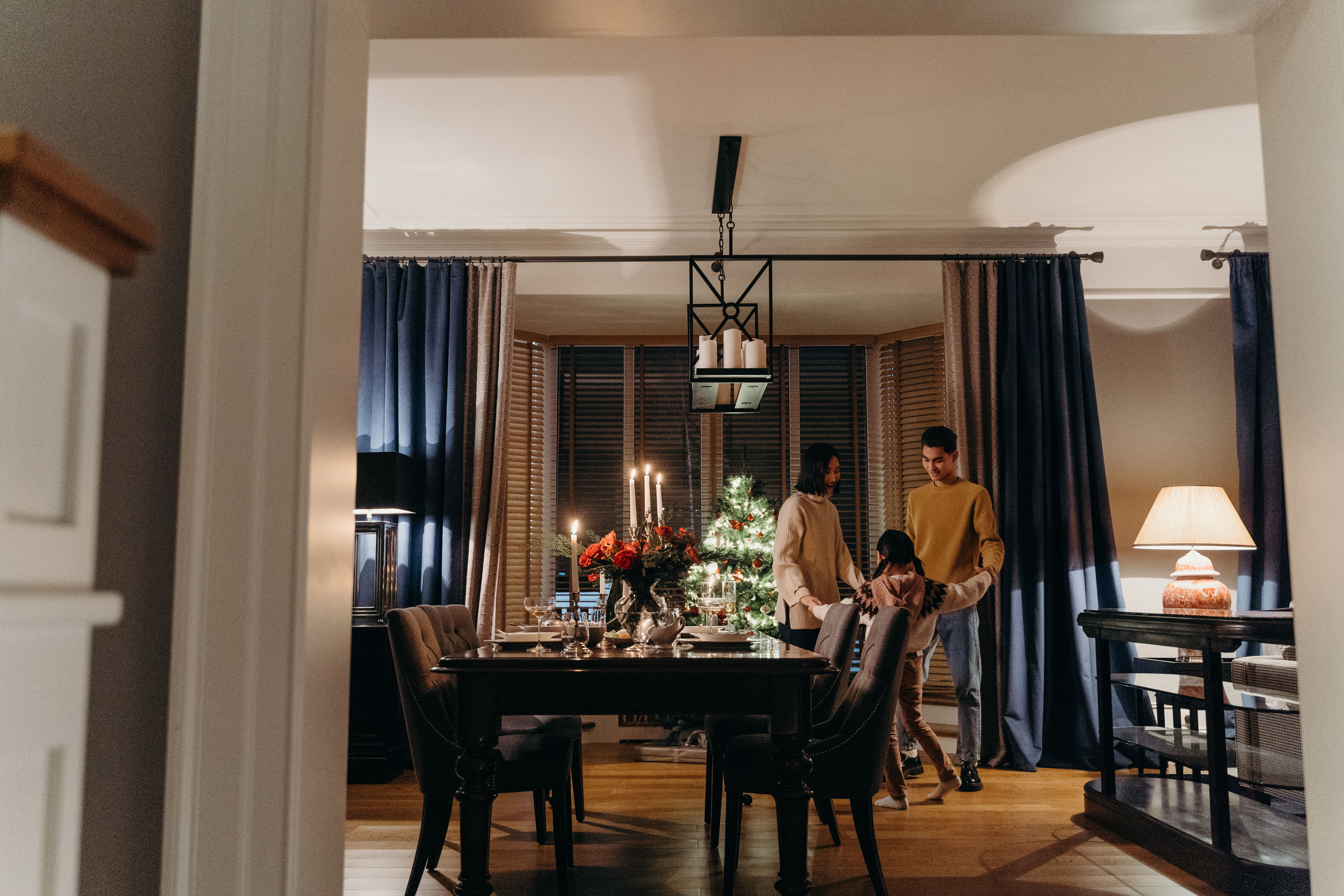 Warm and joyful family gathering around a festive dining table with holiday decorations, candles, and a Christmas tree.