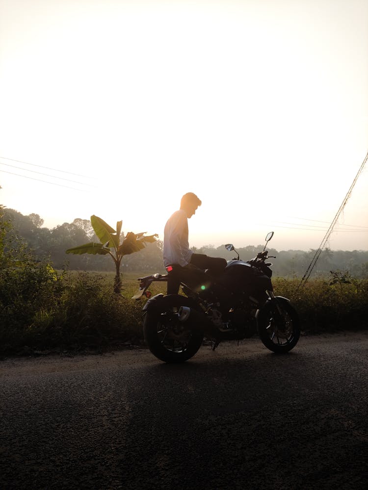 Man By Motorcycle On Road Through Countryside