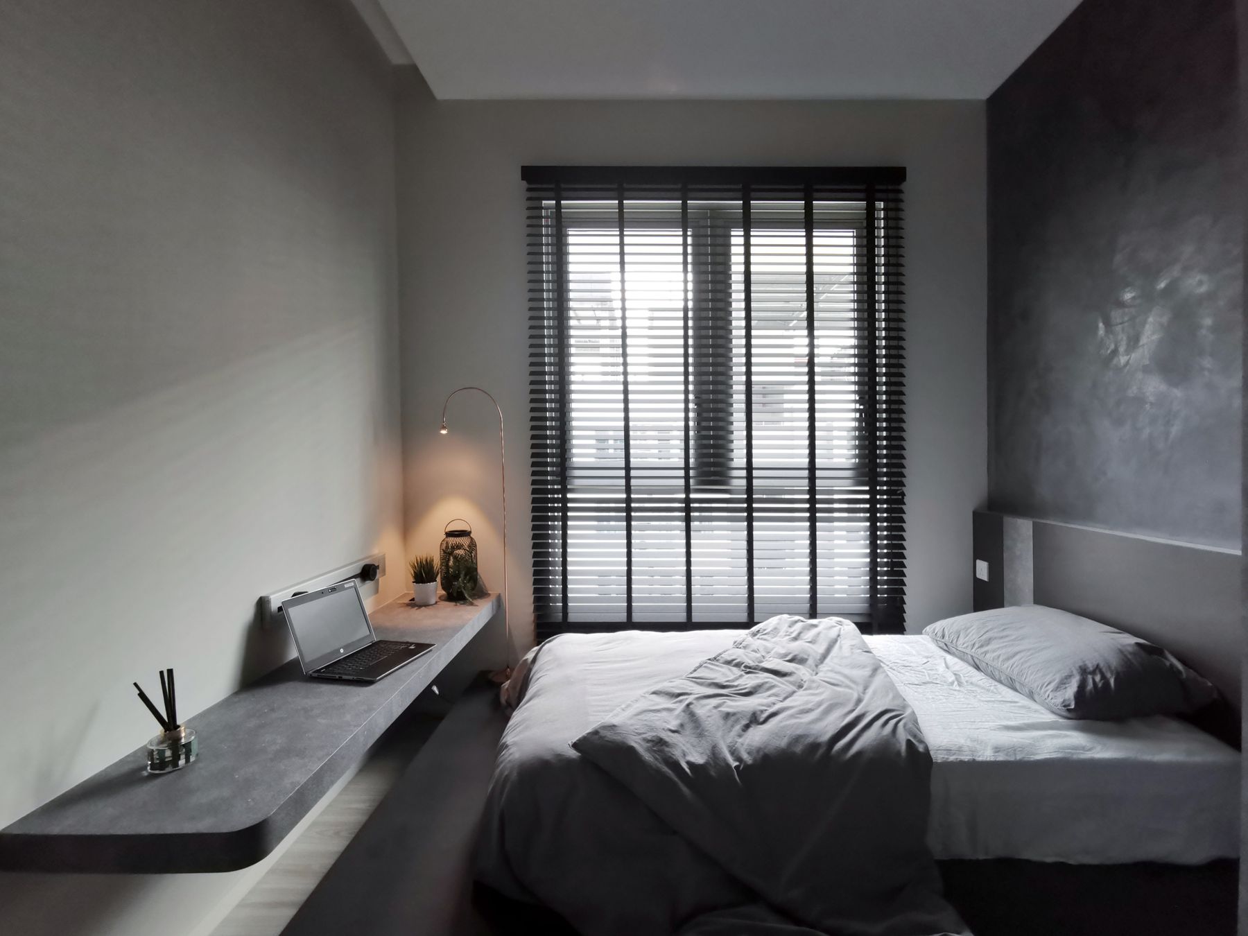 Contemporary gray bedroom with rumpled gray bedding, window blinds and a compact desk with a laptop