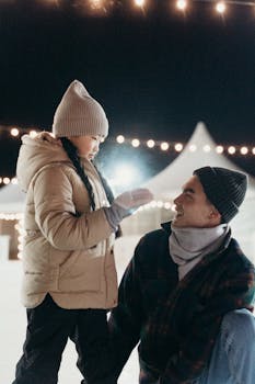 Father and daughter share a joyful moment while ice skating outdoors in winter under festive lights.