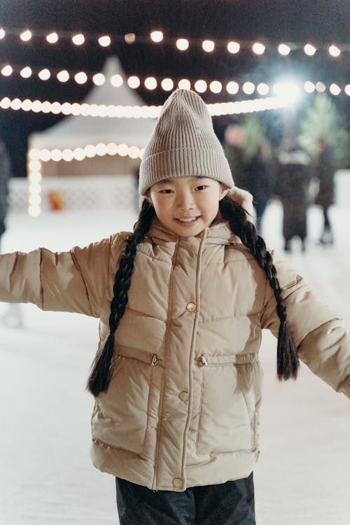A Young Girl Smiling while Wearing a Winter Jacket and a Knitted Cap