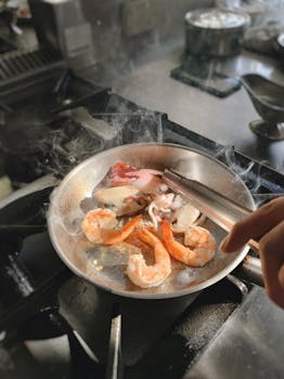 Delicious seafood including shrimp and squid cooking in a frying pan on a stove.