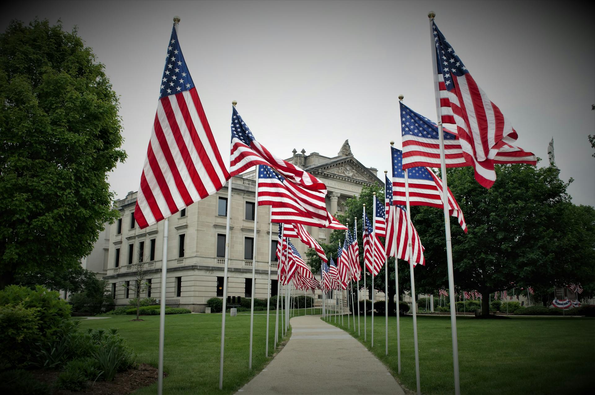 Rows of American flags lining a pathway near a prominent government building during the daytime.