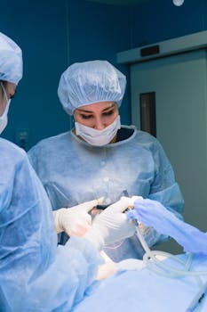 Focused surgeons wearing scrubs and masks conduct surgery in a sterile operating room.