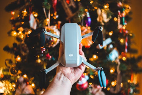 Unrecognizable man showing modern drone near Christmas tree