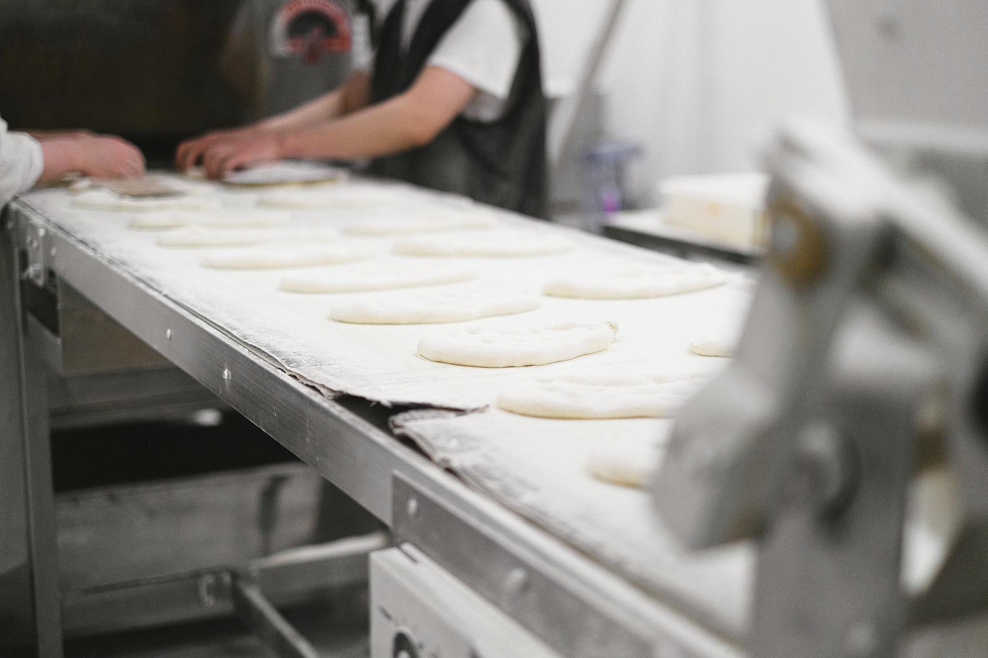 Bakery workers shaping dough pieces on a production line in an industrial setting.