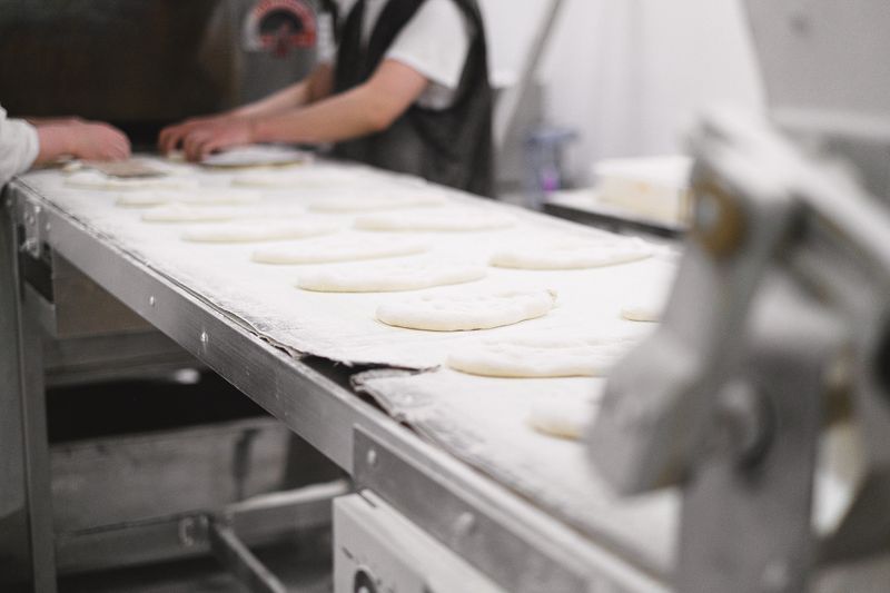 Bakery workers shaping dough pieces on a production line in an industrial setting