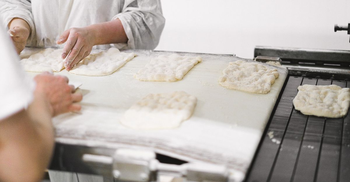 Close-up of bakers shaping dough on a worktable, preparing fresh bread in a bakery.