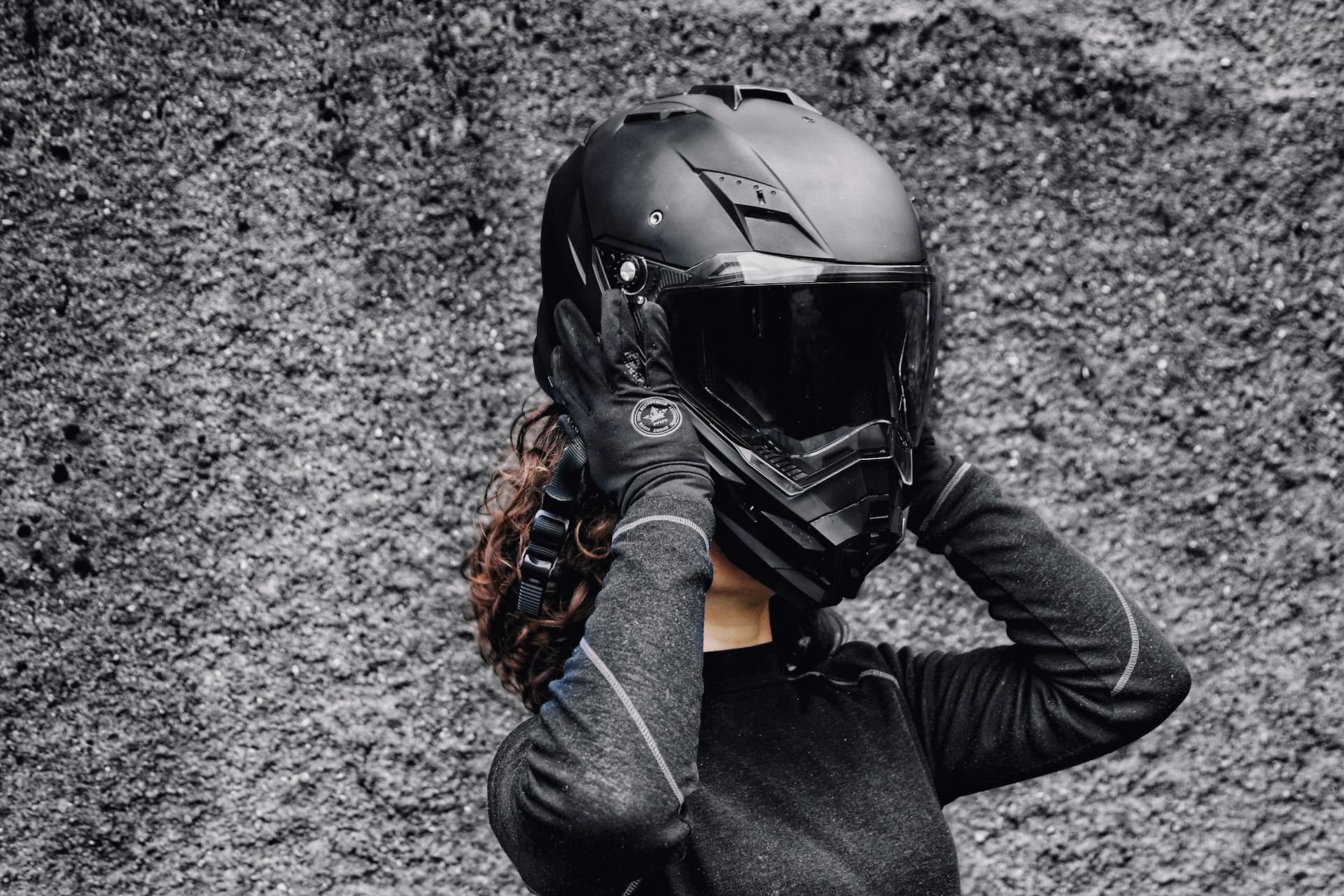 A woman in gloves putting on a motorcycle helmet against a textured background, highlighting safety and adventure.