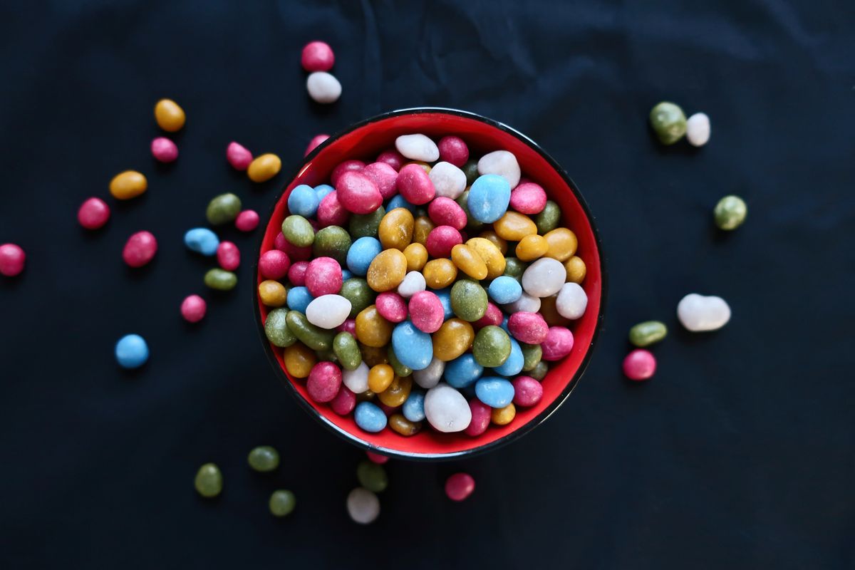 Vibrant assortment of colorful candy beans in a red ceramic bowl, perfect for sweets lovers.