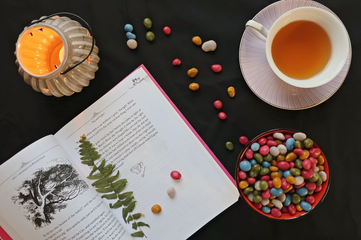 Top view of tea, book, colorful candies, and candle creating a cozy ambiance.