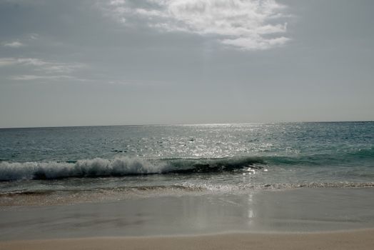 Seascape of waving ocean washing sandy seashore against cloudy sky in sunny tropical country during summer time in coastal area