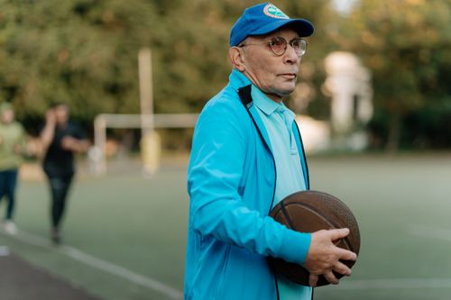Free Elderly man with glasses and cap holding a basketball on an outdoor court. Stock Photo