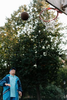 Elderly man in a tracksuit playing basketball outdoors in a park setting.