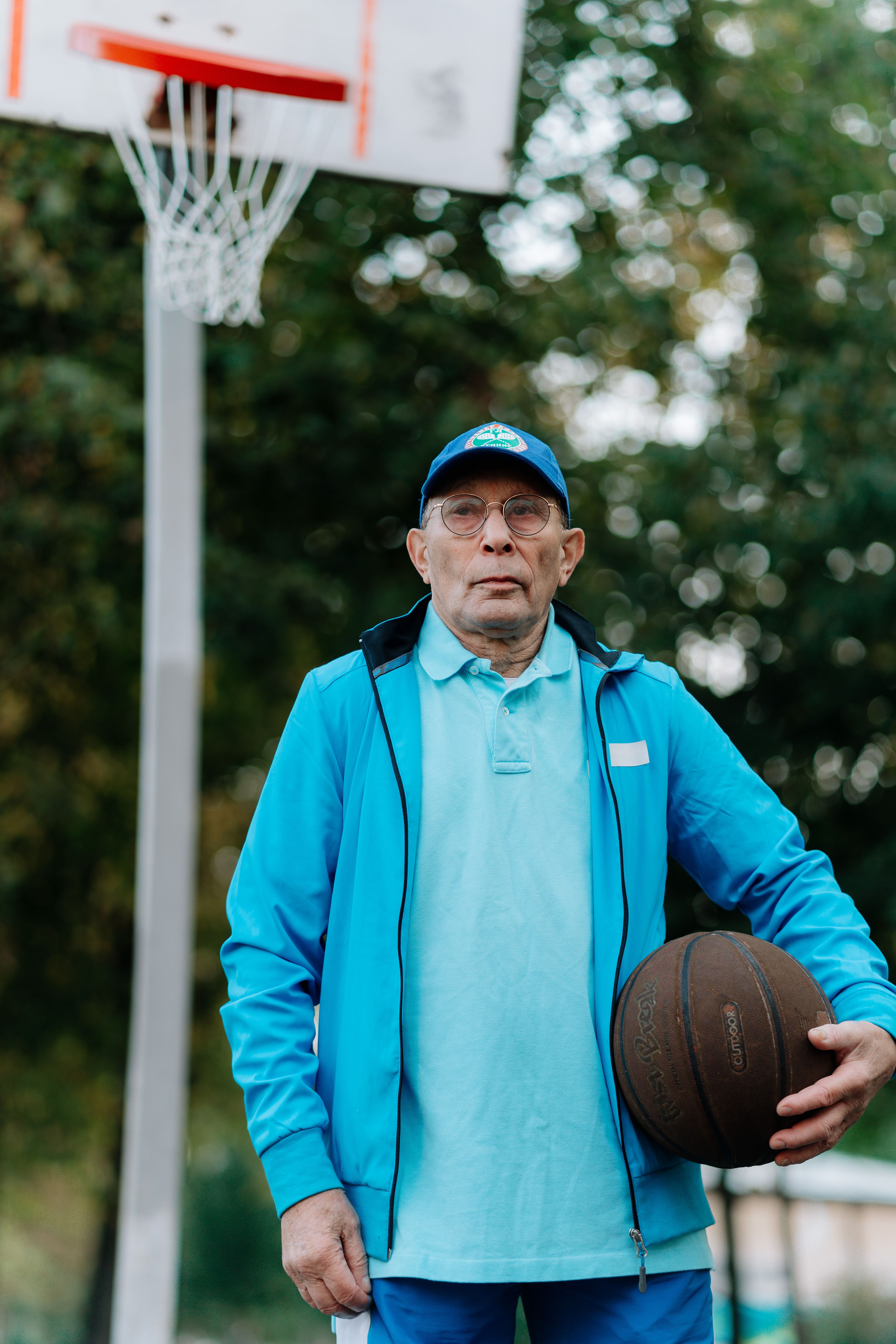 Elderly man in tracksuit holding a basketball on an outdoor court.