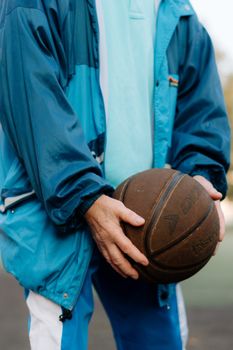 A man holding a basketball outdoors wearing a blue jacket, showcasing casual sports attire.