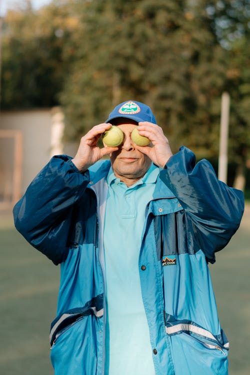 Man in Blue Zip Up Jacket Covering His Eyes with Tennis Ball