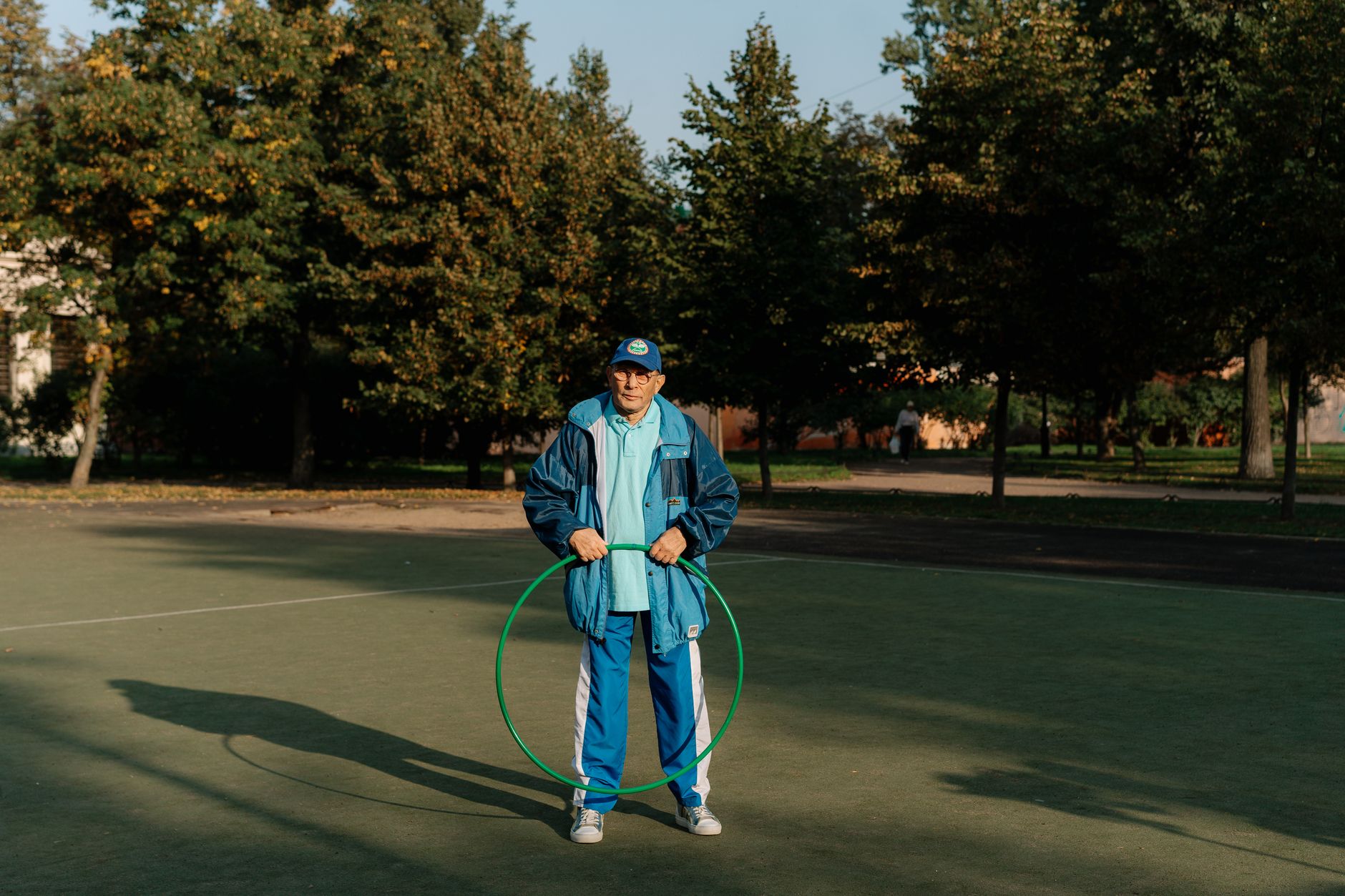 A senior man enjoys leisure time with a hula hoop on an outdoor sports court.