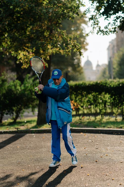 Free An elderly man in a blue tracksuit playing tennis outside on a sunny autumn day. Stock Photo