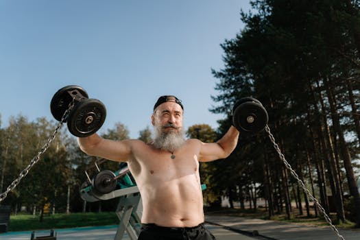 A senior man with a beard exercises shirtless outdoors with dumbbells, emphasizing fitness and determination.
