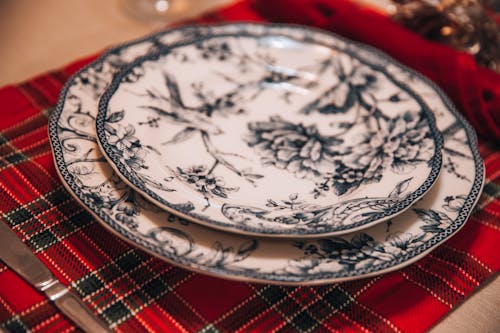 From above of porcelain plate with ornamental elements served on checkered cloth with silverware on table during holiday celebration in room with blurred background