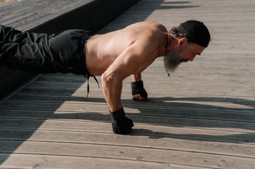Free Senior man with a beard exercising outdoors, performing push-ups on a wooden deck. Stock Photo