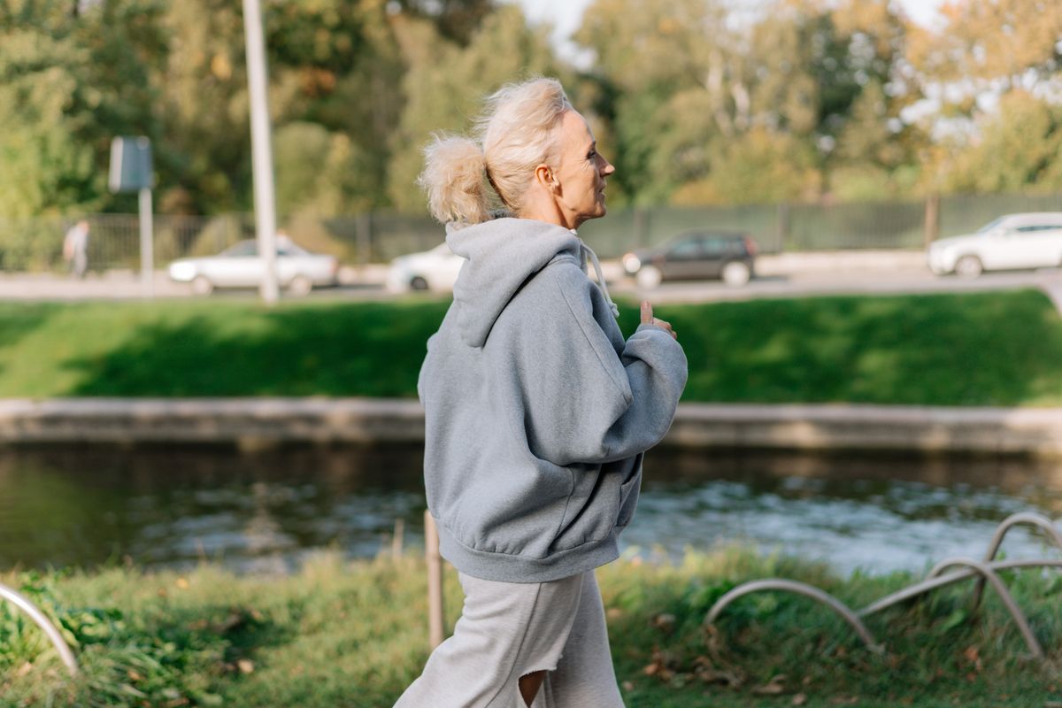 Older woman walking outdoors along a tree-lined path