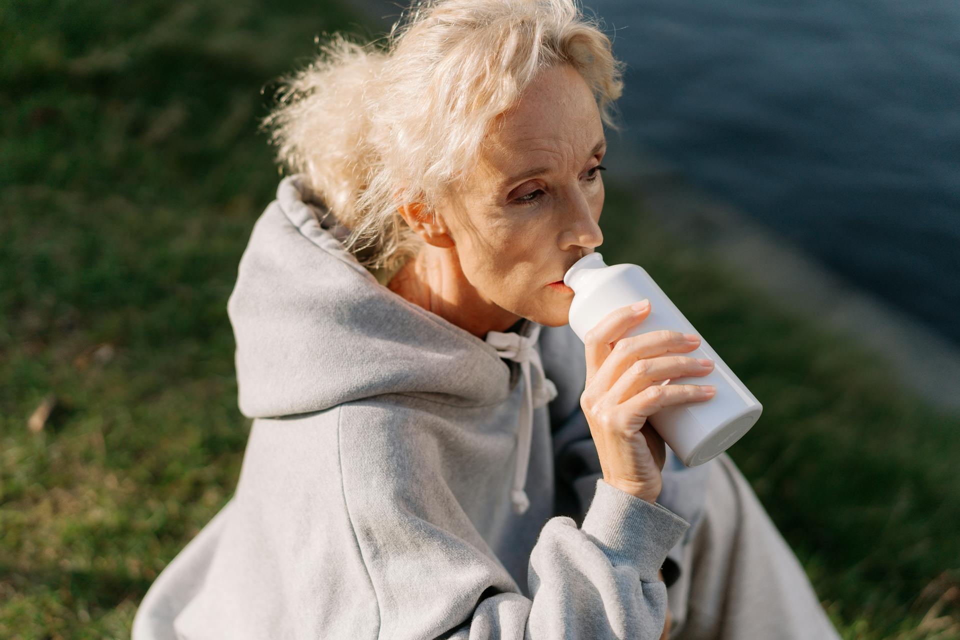 Woman in Gray Hoodie Drinking from White Jar