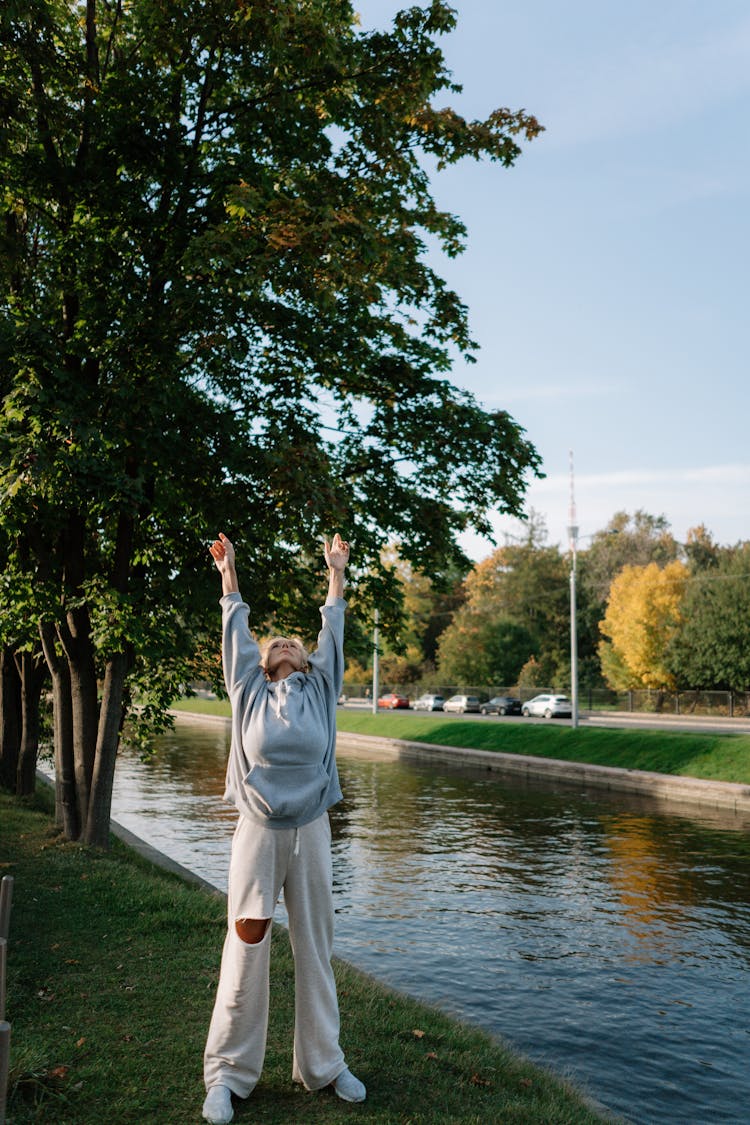 Person Standing On Green Grass Stretching Arms Up 